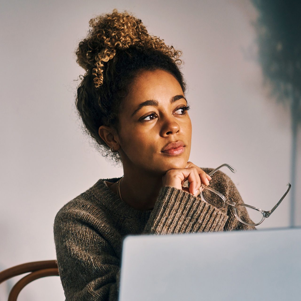 A woman at a laptop, looking away in thought.